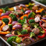 Close-up shot of a colorful sheet pan featuring sausage, broccoli, bell peppers, and red onion.