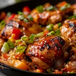 A close-up view of One-Pan Honey BBQ Chicken Rice with glistening chicken pieces, colorful vegetables, and fluffy rice.