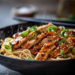 Close-up of Sticky Garlic Chicken Noodles with shiny sauce and garnished with green onions.