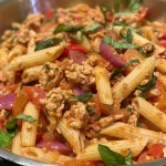 Close-up of ground chicken mixed with whole-wheat penne pasta, garnished with fresh basil.