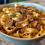Close-up view of a hearty bowl of beef and noodles topped with fresh herbs.