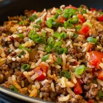 Close-up view of a bowl of Dirty Rice topped with ground beef and green onions.