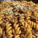 A close-up view of creamy ground beef pasta with diced tomatoes and garnished with parsley.