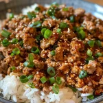Close-up view of a bowl filled with healthy ground turkey and rice, garnished with green onions and sesame seeds.