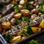 Close-up of a sheet pan featuring steak, diced potatoes, and broccoli, beautifully lit.