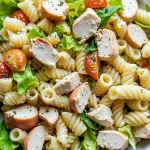 Close-up of a creamy chicken Caesar pasta salad with rotini, diced chicken, romaine lettuce, cherry tomatoes, and parmesan cheese.
