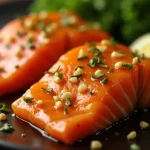 Close-up view of honey garlic glazed salmon fillets served with lemon wedges and garnished with green onions.