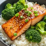 Close-up of a honey garlic salmon rice bowl topped with sesame seeds and green onions.