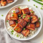 Close-up of honey garlic salmon bites garnished with green onions and lemon wedges.