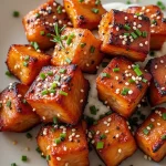 A close-up of crispy honey garlic salmon bites served on a wooden plate with green onions.