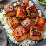 Close-up view of honey garlic salmon bites on a rustic plate, garnished with green onions.