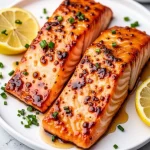 Close-up of a beautifully plated honey garlic salmon fillet with a golden glaze and lemon wedges.