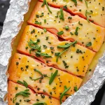 Close-up of honey garlic butter salmon fillets in foil with herbs and lemon.