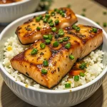 Close-up shot of a bowl featuring honey garlic salmon, rice, broccoli, and carrots, beautifully arranged and garnished.