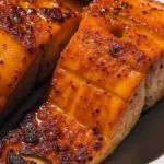 Close-up of golden-brown Air Fryer Honey Garlic Salmon fillet garnished with green onions and lemon wedges.