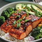 A close-up of a honey garlic salmon bowl featuring salmon fillets, broccoli, avocado slices, and sesame seeds on brown rice.