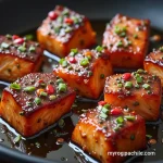 Close-up view of crispy honey butter glazed salmon bites on a plate, garnished with green onions.