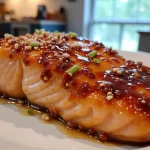 Close-up of Honey Garlic Glazed Salmon garnished with green onions and sesame seeds.