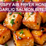 Close-up of crispy honey garlic salmon bites garnished with sesame seeds and green onions.