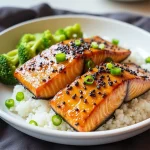 Close-up of honey garlic salmon fillet, glistening with sauce and garnished with green onions.