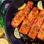 Close-up of honey garlic salmon fillet garnished with sliced green onions on a wooden plate.