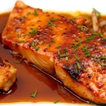 Close-up shot of honey glazed salmon fillets, garnished with lemon slices and fresh dill.