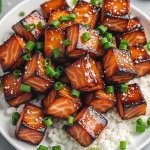 Close-up of honey garlic salmon bites coated in a glossy sauce, garnished with green onions.