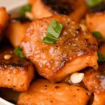 Close-up image of honey-glazed salmon bites with garlic on a wooden plate.