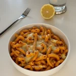 Close-up shot of cheesy chicken pasta with shredded cheese and herbs.