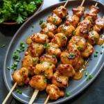 Close-up of golden-brown Bang Bang Chicken skewers garnished with green onions.
