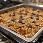 Close-up view of a slice of baked chocolate chip oatmeal with chocolate chips on top.