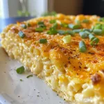 Side view of a savory mac and cheese cake topped with melted cheese and garnished with green onions.