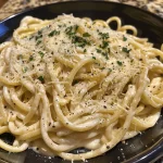 Close-up view of creamy spaghetti Alfredo topped with Italian sausage and herbs.