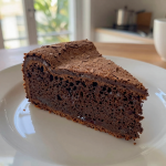 Close-up of a glossy, dark chocolate cake on a wooden table.