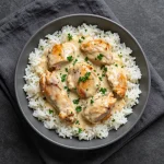 A close-up of a skillet filled with creamy smothered chicken and rice, garnished with fresh parsley.