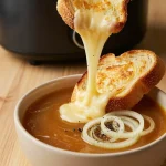 A bowl of steaming French onion soup topped with melted cheese and fresh herbs, served with a slice of crusty bread.