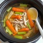 A bowl of classic chicken soup garnished with parsley, served with a slice of bread