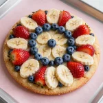 A gluten-free flag fruit pizza decorated with blueberries, strawberries, and bananas to resemble the American flag.