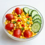 A vibrant bowl of fresh corn salad with tomatoes, cucumbers, and parsley.