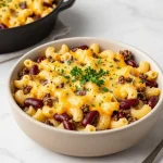 A creamy bowl of chili mac and cheese topped with fresh herbs